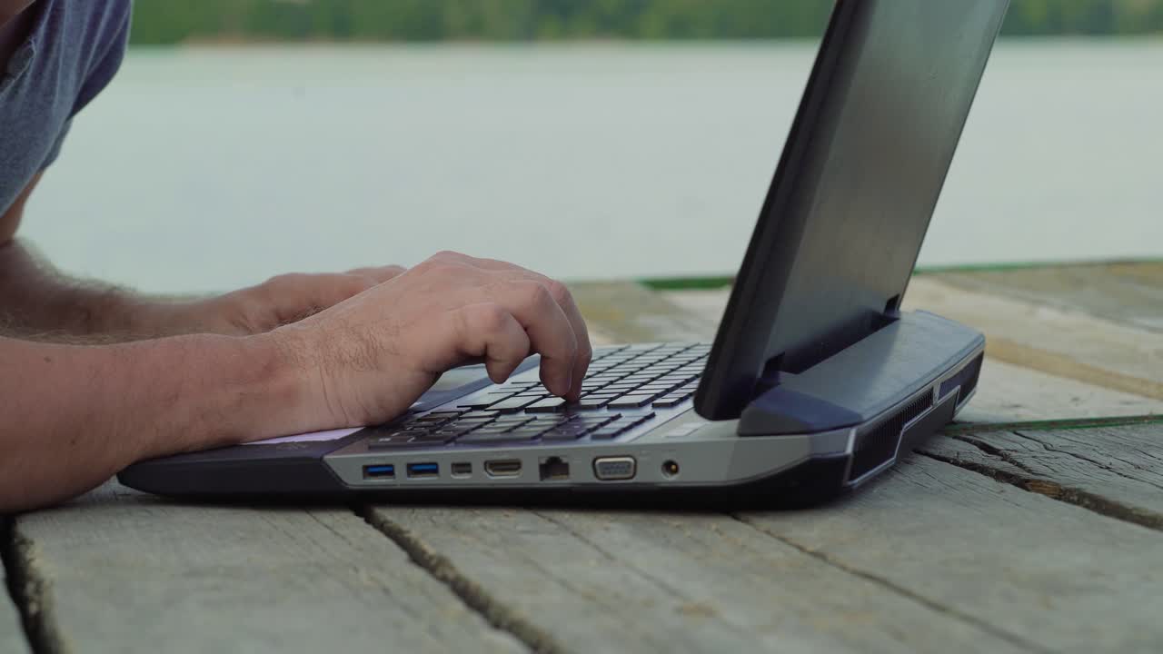 Man's hands using laptop computer. Young man sitting on a wharf and using a notebook