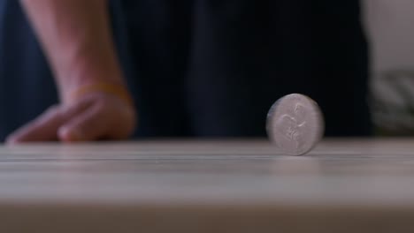 big coin spinning in and back out from right to left on wooden table, macro slow motion