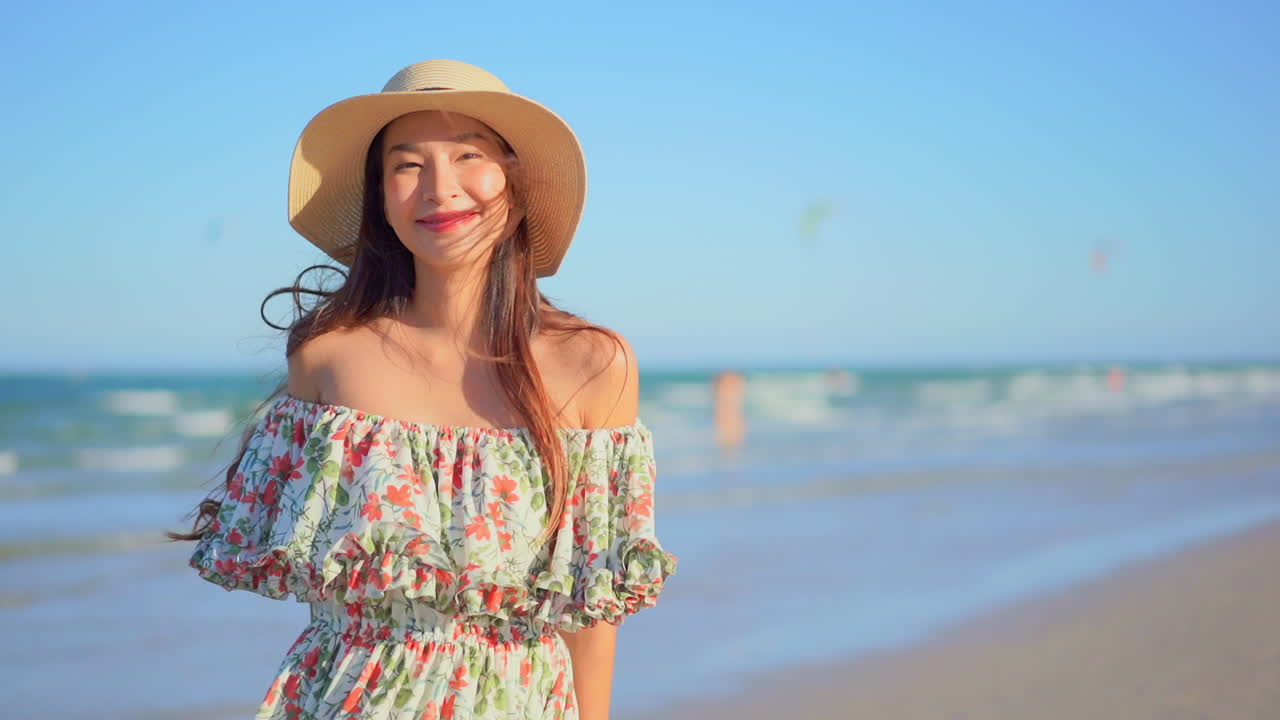 Pretty young Asian lady smiles looking at camera at beach, medium shot