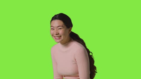 studio portrait of woman smiling and laughing standing against green screen