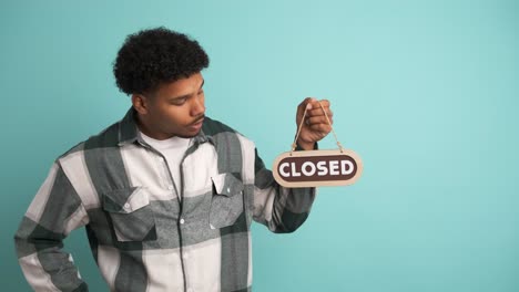 upset young man with closed sign in blue studio