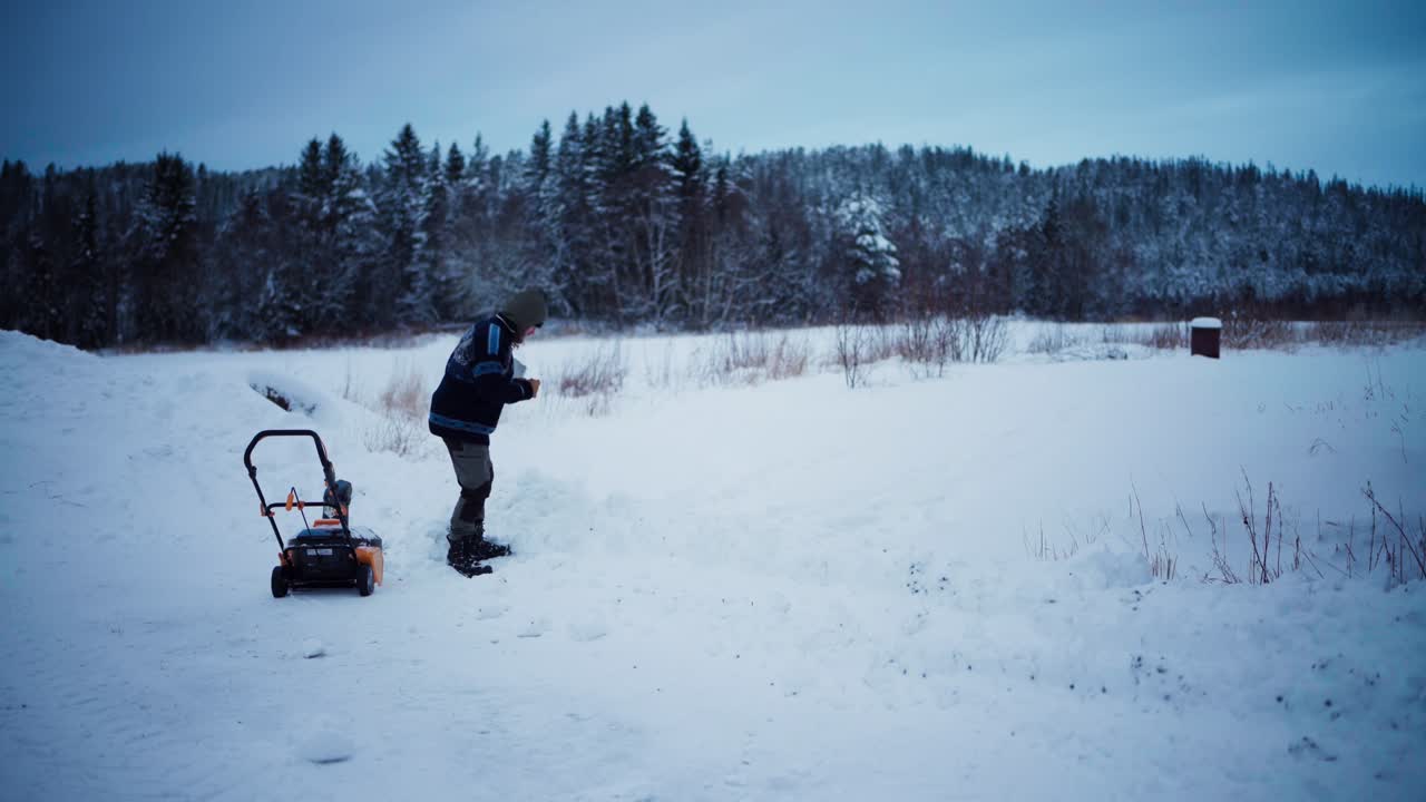 Person arbejder i vinterlandskab med sneblæser og skovl