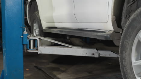 detailed close-up of a white suv being securely lowered from a hydraulic lift in an auto repair shop, focusing on the vehicle's side and lift mechanism