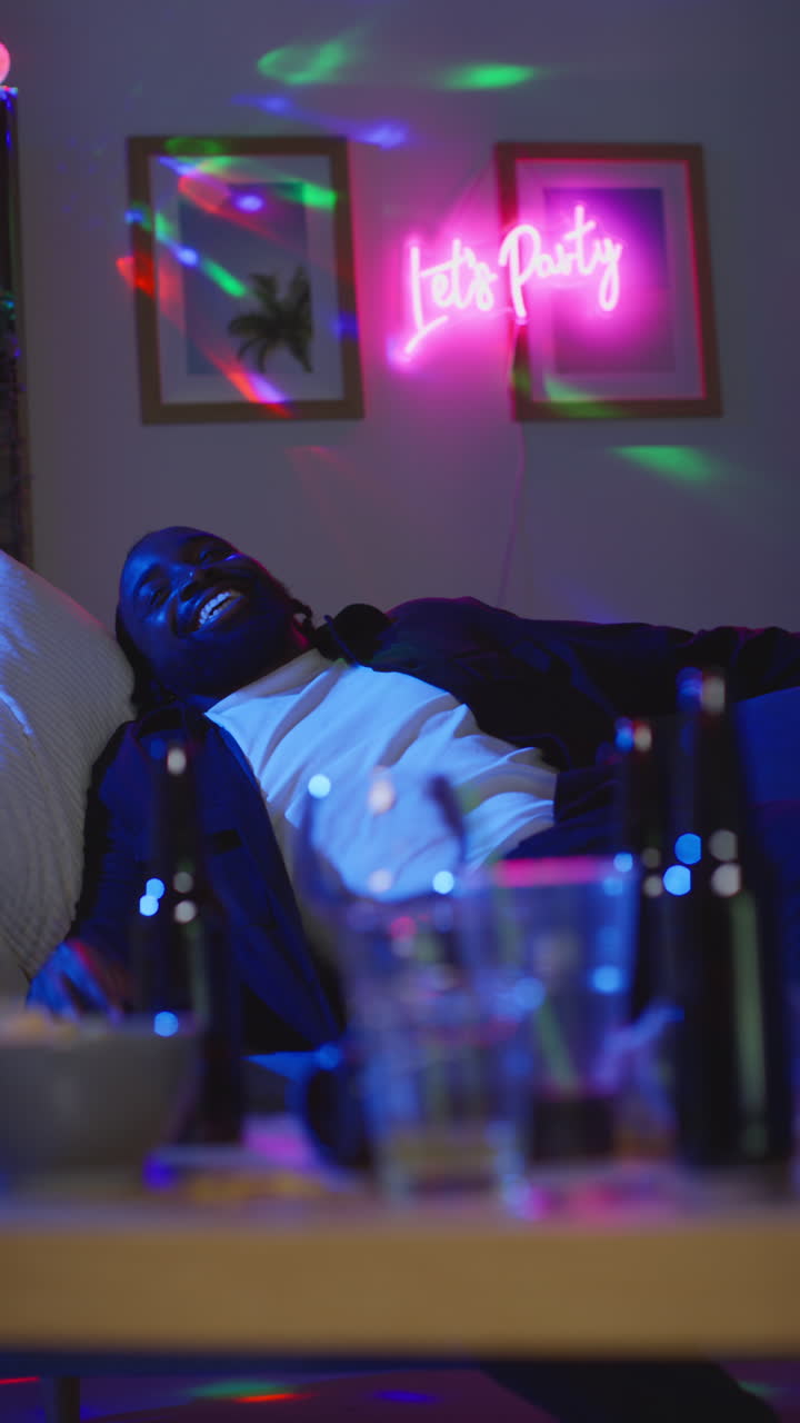 video vertical de un hombre borracho sentado en el sofá bebiendo alcohol en una fiesta en casa