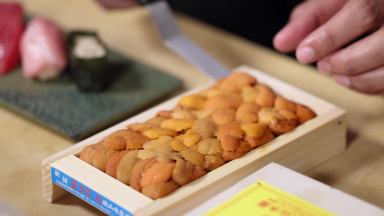 Close-up shot of a chef's hand carefully lifting fresh uni from a wooden tray