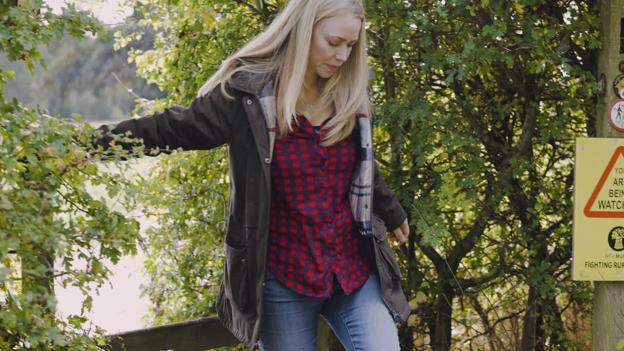 Woman in jacket climbing over a wooden fence in a rural area