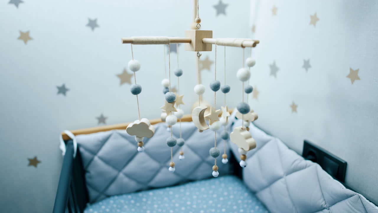 Cozy empty bed with soft sides for a baby boy. Nursery crib mobile of natural materials is hanging above the cot.