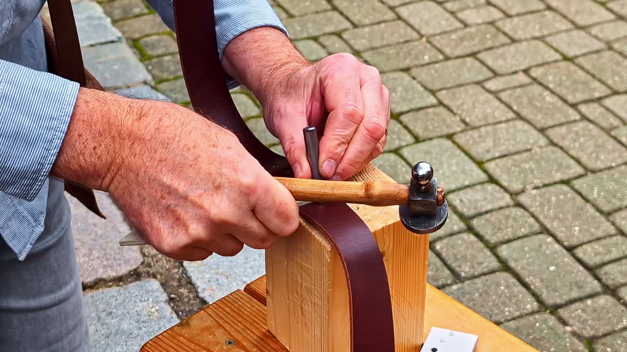Persona che pratica un foro in una cintura di pelle usando un martello e uno strumento di metallo all'aperto