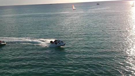 Aerial-shot-focused-on-a-sports-boat-pulling-a-donut-float-with-people-on-it,-ath-sunset-in-a-paradise-island