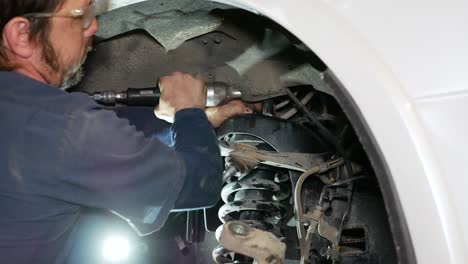 a mechanic seen tightening the nuts for a front strut on a vehicle.