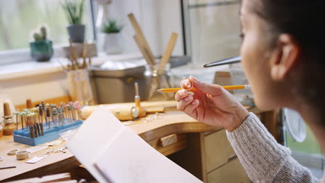 close up of female jeweller sketching out design for ring in studio