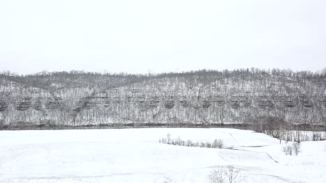 Disparo-De-Drones-Moviéndose-Hacia-Algunas-Colinas-Cubiertas-De-Nieve-Junto-A-Un-Río