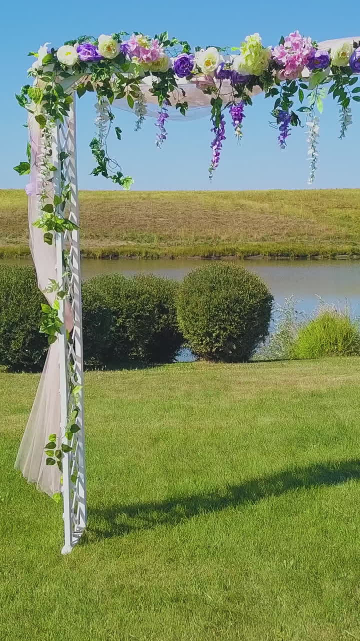 wonderful wedding arch decorated with fresh flowers on green lawn near calm river in early autumn close motion