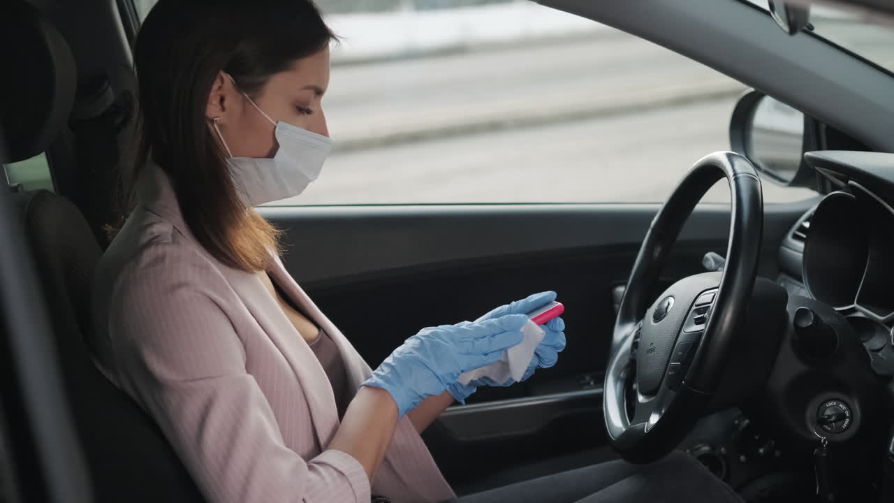 mujer conduciendo y desinfectando el teléfono en un coche