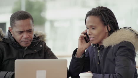 Afro-American middle-aged man in black jacket with fur hood and Afro-American young girl with braids calling friend to receive more details