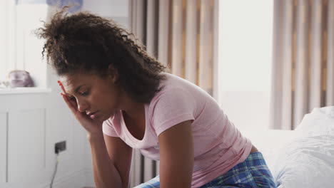 woman wearing pajamas suffering with depression sitting on bed at home