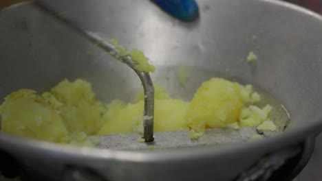 a chef using a knife to cut up cooked potatoes and a steel mouli to puree them using the wooden handle to turn the mill