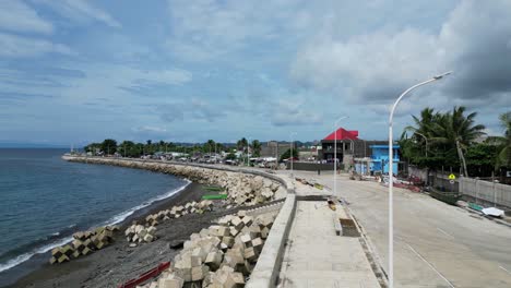 establishing shot of extensive, island seawall with white lamp posts and roads, protecting tropical village town