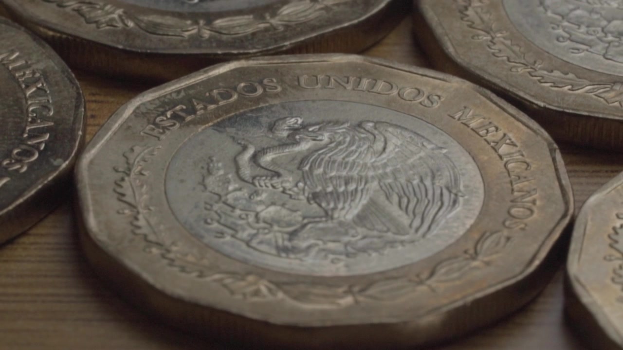 Primer plano de monedas de peso mexicano con el escudo nacional con el diseño del águila y la serpiente, dispuestas sobre una superficie de madera en México