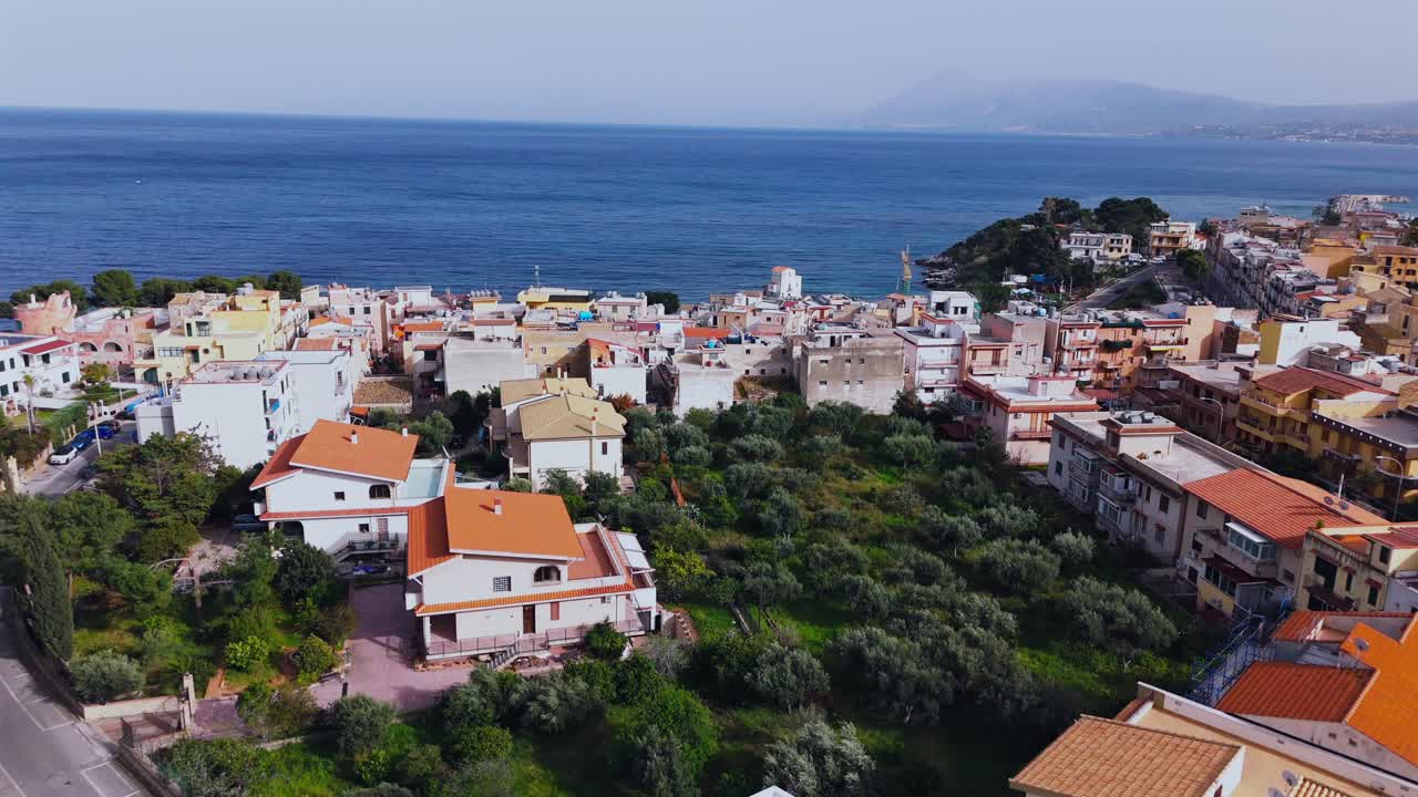 Drone flies slowly above red-roofed homes and olive groves in Porticello, Sicily, revealing coastal village structures and the Mediterranean Sea near Palermo and Santa Flavia