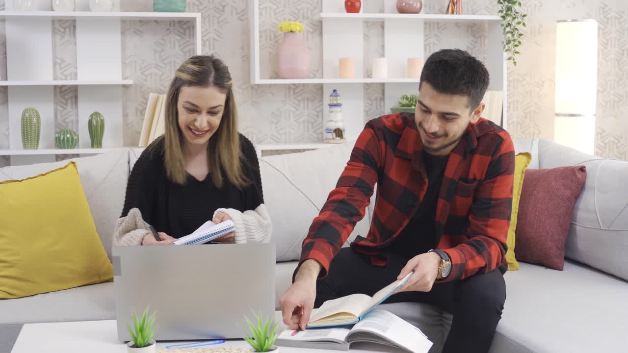 un joven y una mujer enamorados están estudiando en casa usando una computadora portátil.