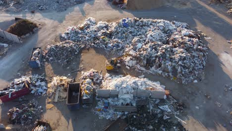 excavator moving waste materials at a landfill site on a sunny evening