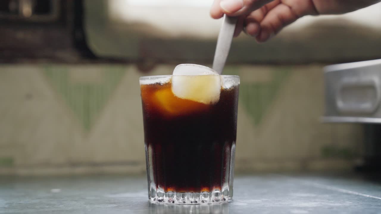 A closeup footage of stirring the ice cubes in an iced tea glass with a small stainless steel knife
