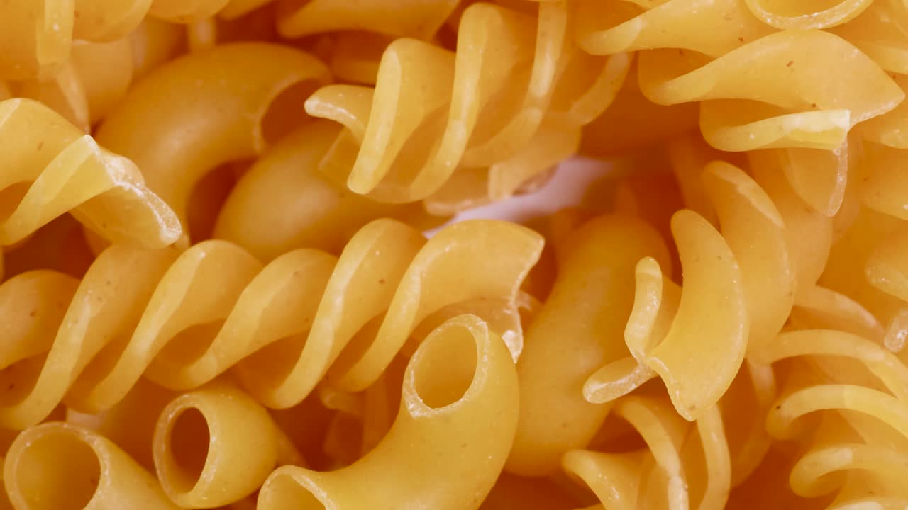 Close-up video of spiraling and elbow pasta falling, showcasing texture and movement under bright lighting