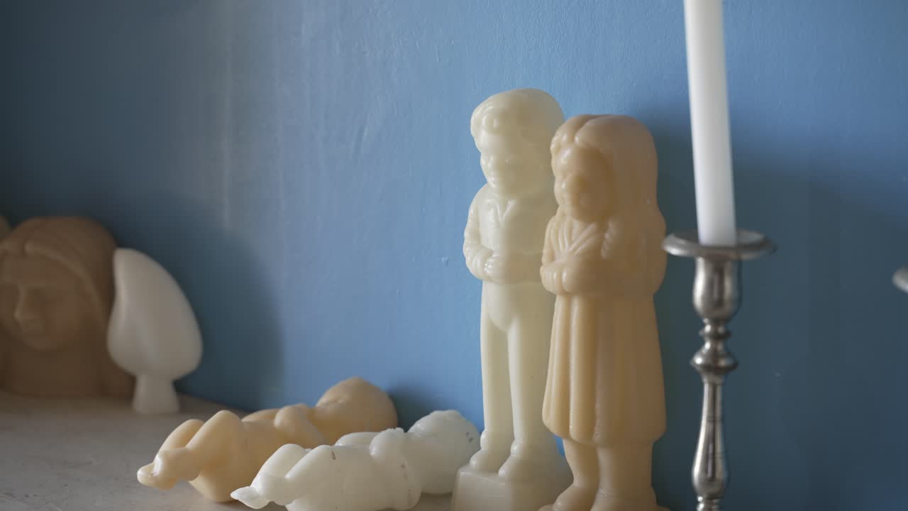 figuras de cera de niños y bebés en un estante con un fondo de pared azul y un candelabro de plata