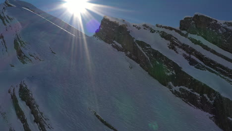 vista aérea alejándose de un sombrío valle montañoso con sol en la toma creando un destello de luz en los alpes franceses en invierno