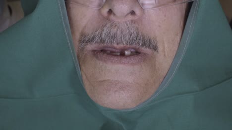 older man missing a tooth, covered with a green surgical cloth, preparing for treatment