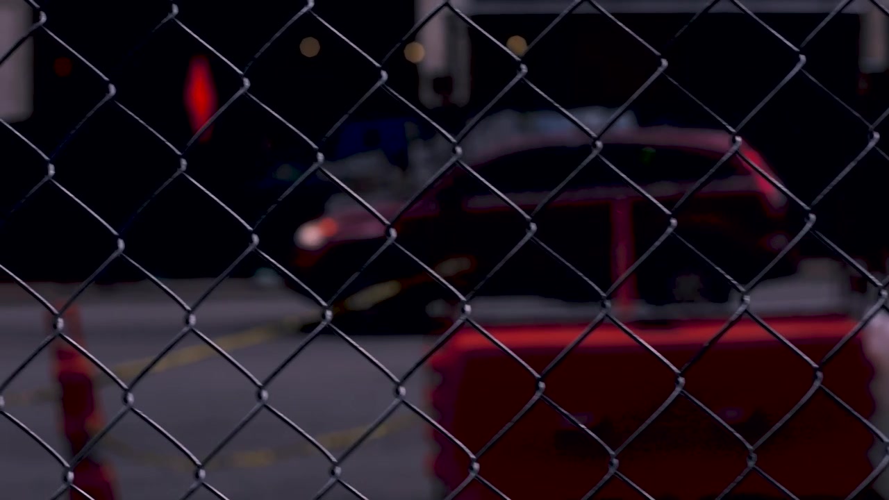 Slow motion shot of car through wire fence driving down a city street.