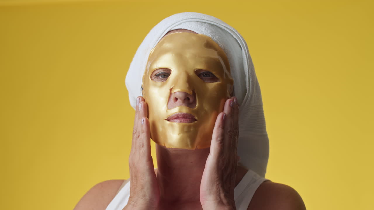 Kvinne med ansiktsmaske påført på ansiktet på gul bakgrunn