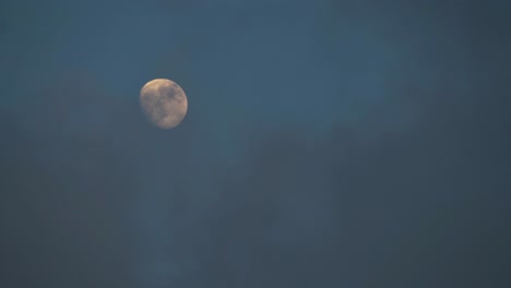 clouds slowly cover illuminated waxing gibbous moon at dusk