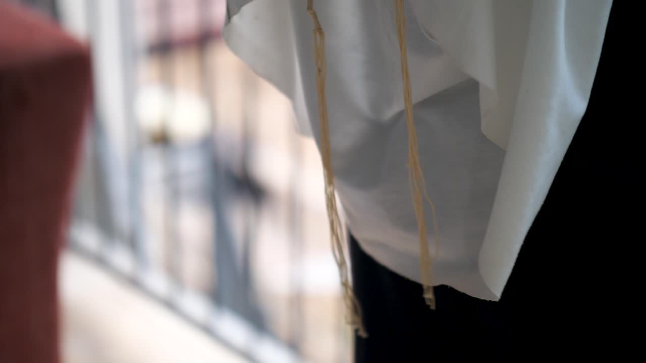 Primo piano di tzitzit che ondeggiano delicatamente durante un rituale di preghiera ebraica.