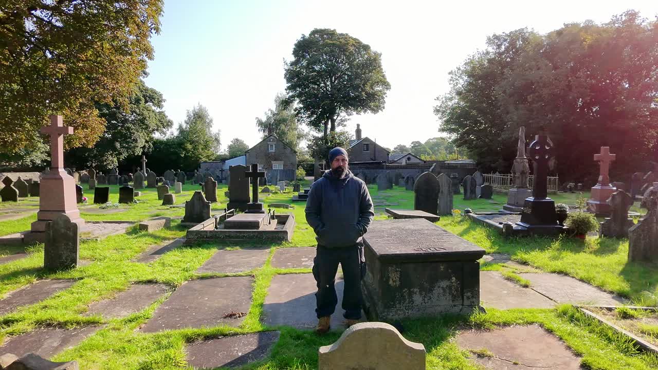 Male wearing hat and casual clothing alone in peaceful sunlit cemetery aerial orbiting view