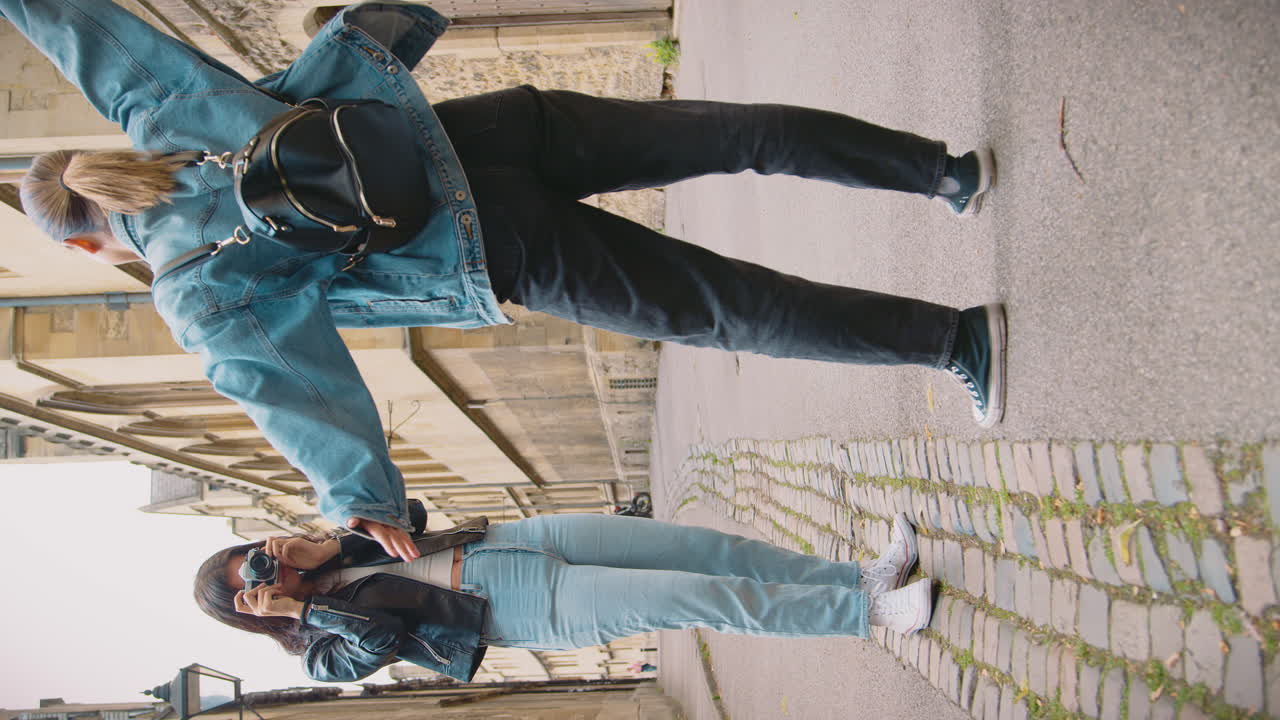 video vertical de una pareja de mujeres del mismo sexo tomando fotos la una de la otra en una cámara digital retro