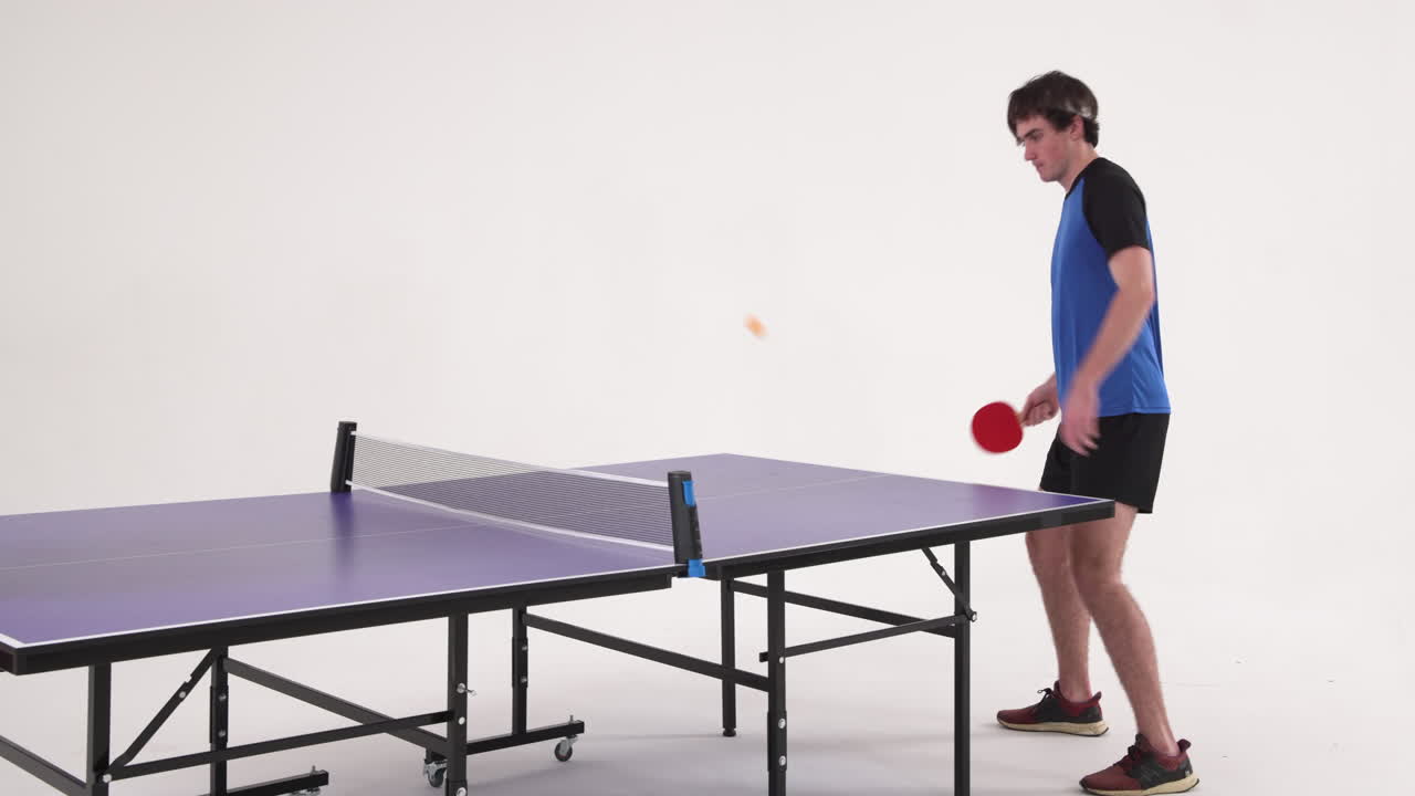 Playing table tennis, man hitting ball with paddle in studio setting