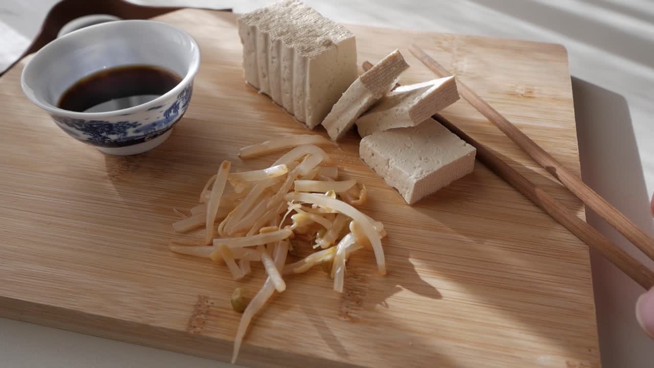 Sliced tofu with bean sprouts, soy sauce, and chopsticks on a wooden board