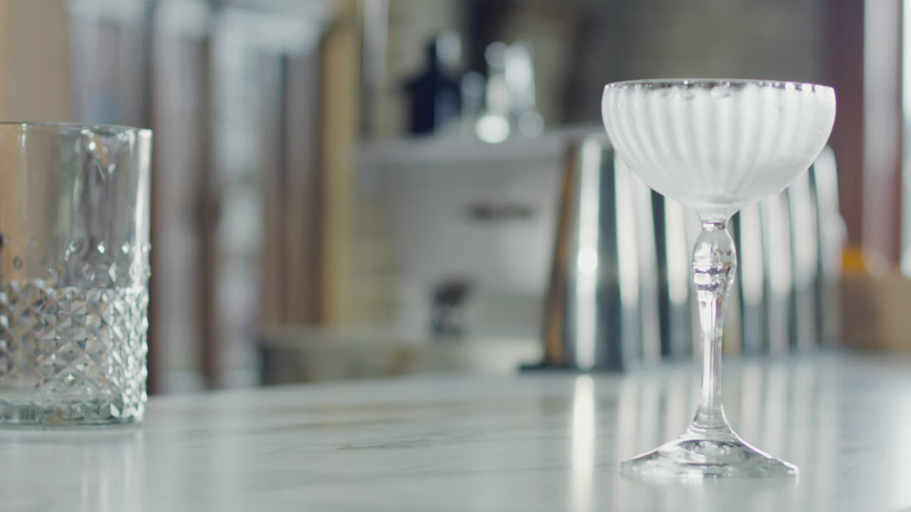 Close-up of a glass as the bartender pours liquor from a jigger to prepare a cocktail