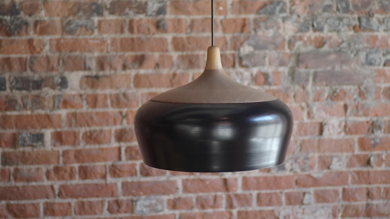 Modern Black and Wood Pendant Light Swaying in Front of a Brick Wall