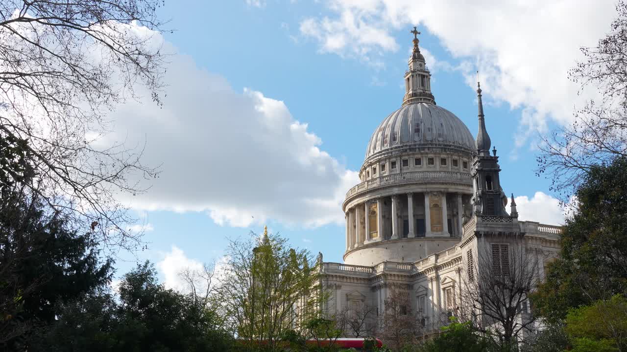 Catedral de St Paul em Londres com vista para a cúpula e as árvores circundantes. Cena diurna mostrando arquitetura histórica e nuvens no céu.