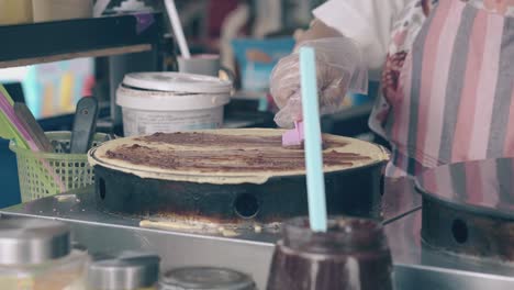 woman covers pancake with chocolate on crepe maker in cafe