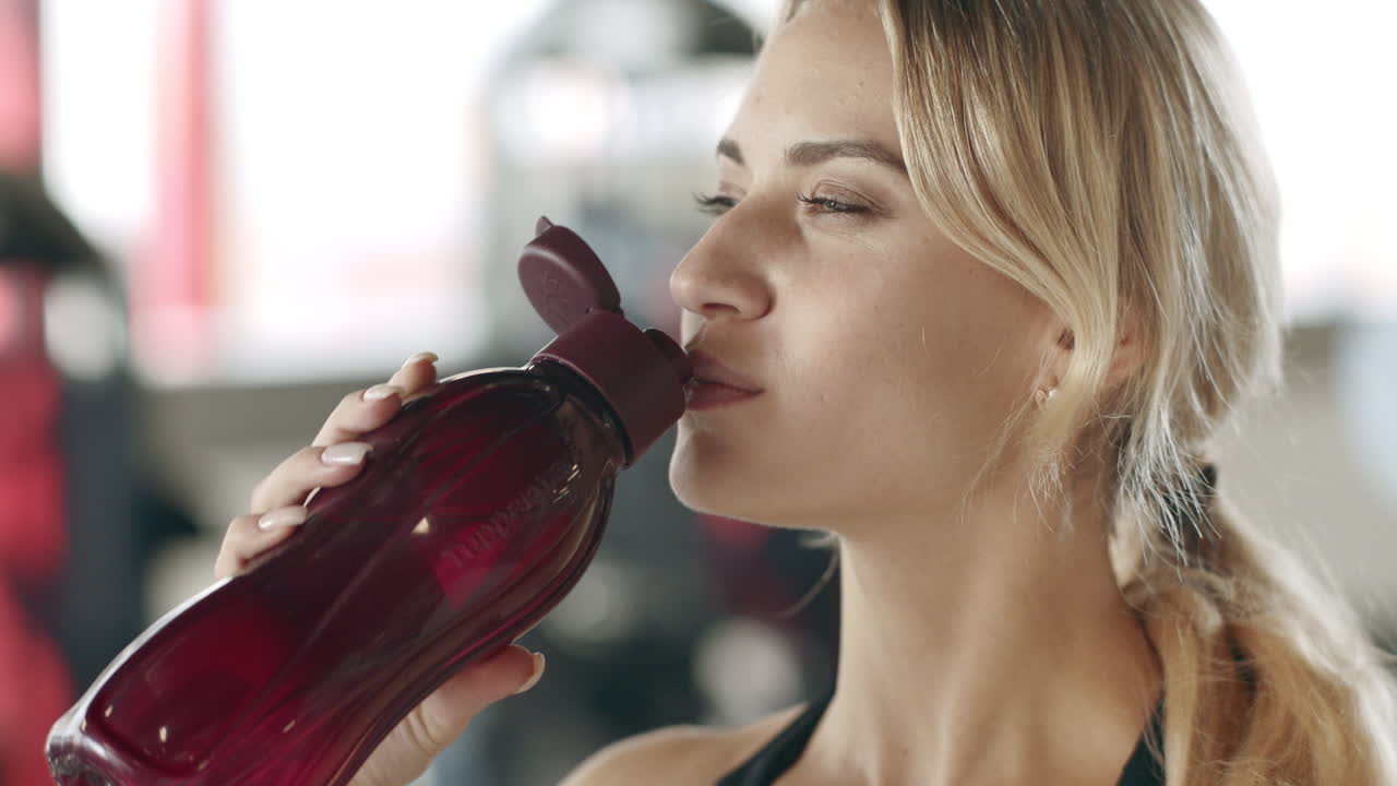 mujer deportiva sonriente bebiendo agua en el gimnasio. niña feliz bebiendo agua