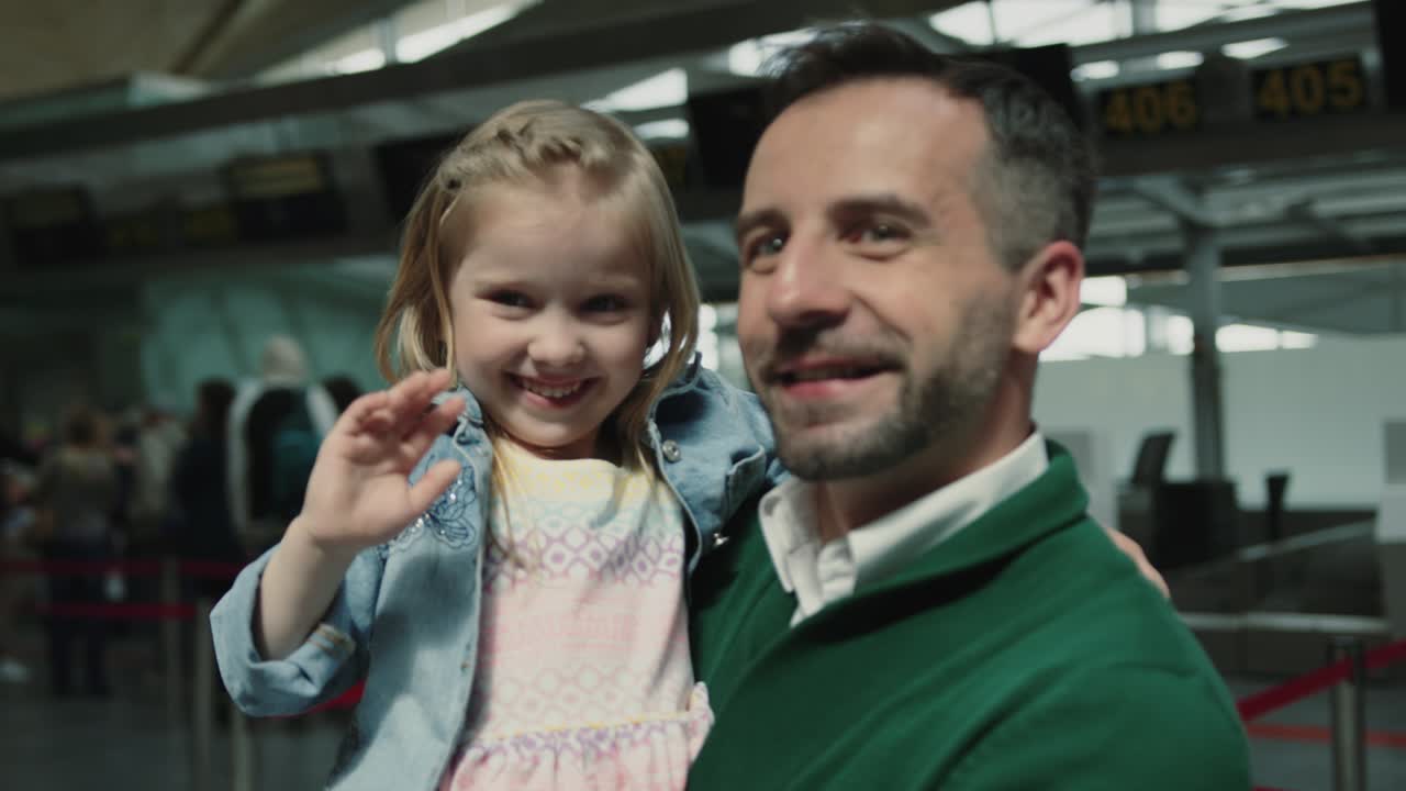 행복한 귀여운 어린 소녀와 아빠가 엄마를 기다리고, 딸이 손을 흔들고, 인사합니다. 공항 터미널. 빨간 카메라에서 영화 촬영.