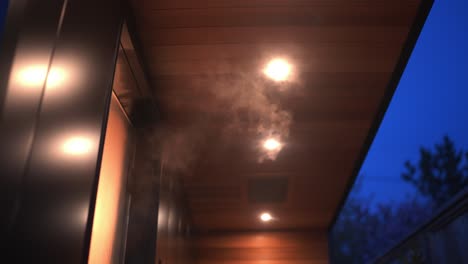 close up of steam escaping from an outdoor luxury sauna in the evening with warm top down lights glowing