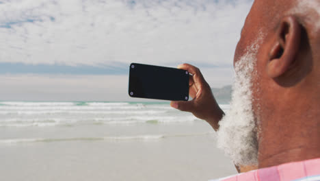 hombre de edad avanzada de raza mixta tomando una selfie con un teléfono inteligente en la playa