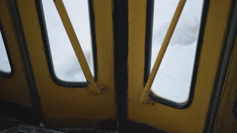 low interior view of locked yellow train door with metal supports and frosted glass, motion blur outside on winter snow as carriage rolls forward, hinges and frame visible during ride