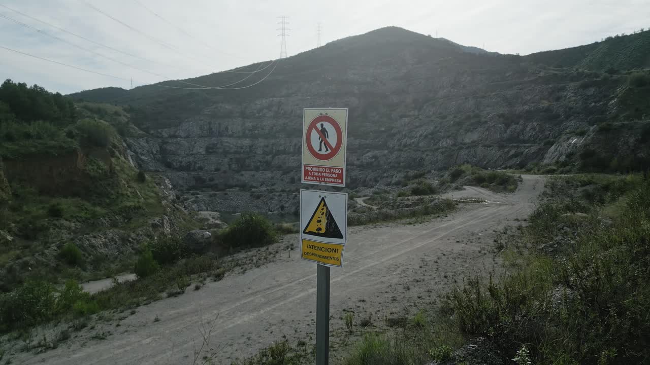 Warning signs blocking quarry entrance highlighting falling rocks danger, preventing unauthorized personnel access and emphasizing industrial workplace safety precautions, spanish language