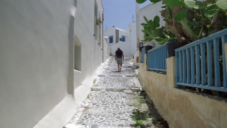 siguiendo a un hombre caminando por una calle estrecha de una isla griega en un día soleado